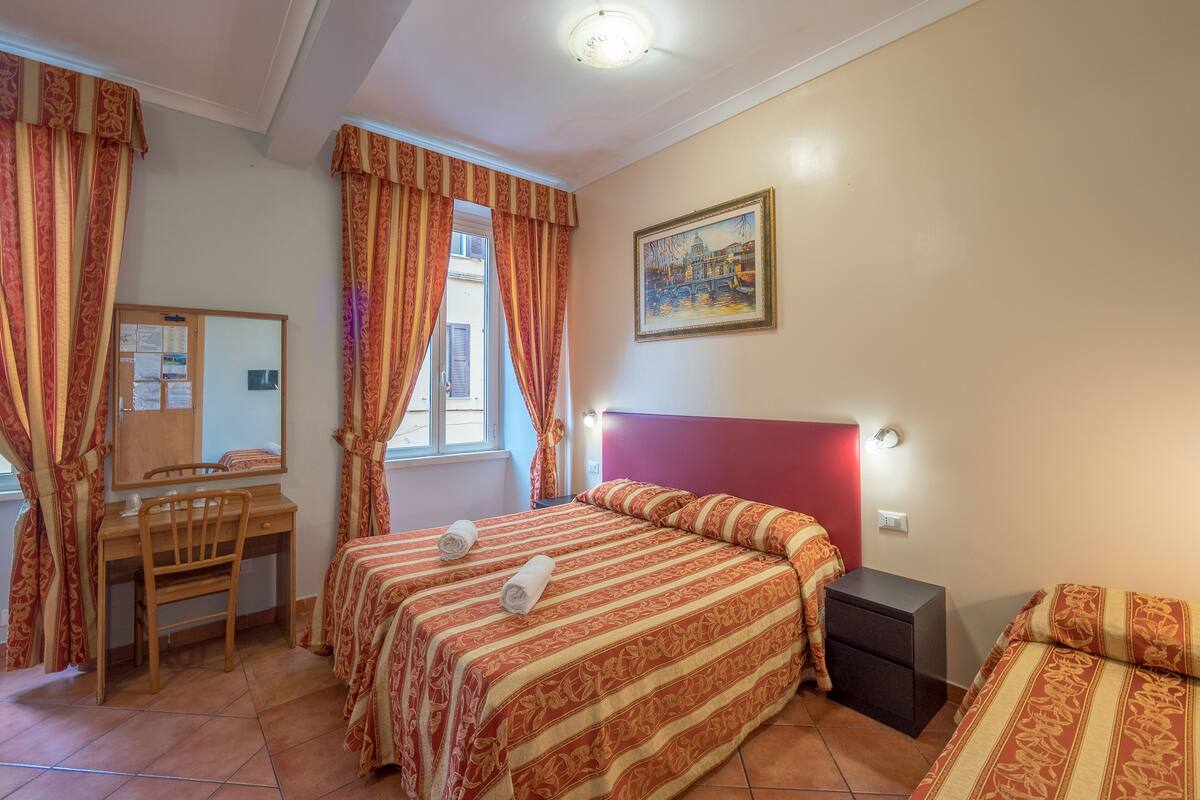 A bedroom with two beds, a desk, a chair, a nightstand, and a painting on the wall.