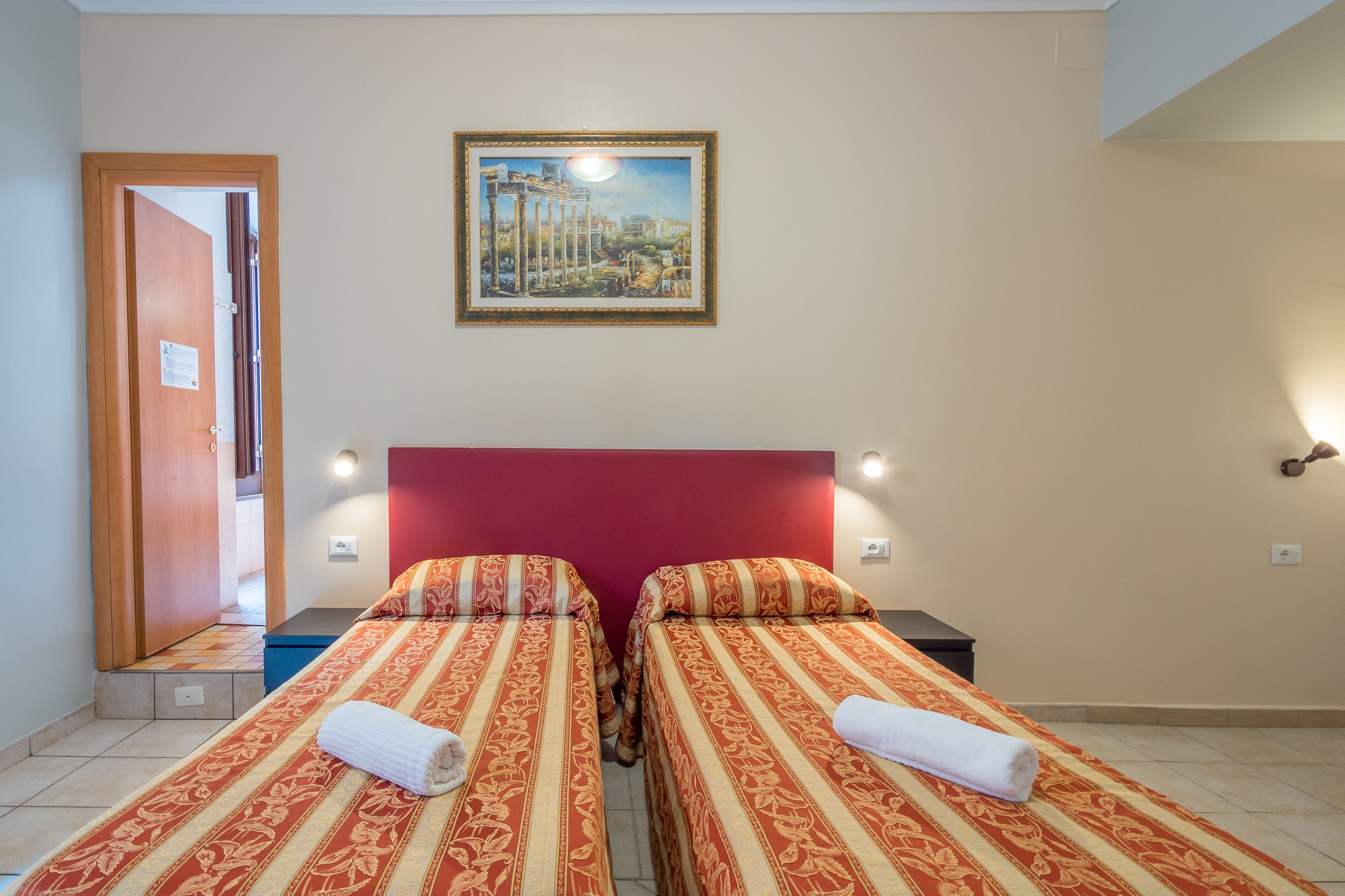 Una habitación de hotel con dos camas, un cabecero rojo y un cuadro sobre las camas.