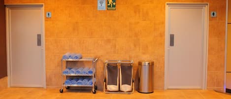 A hotel lobby with two doors, a towel rack with towels, a waste bin, and a sign indicating free Wi-Fi and an emergency exit.