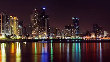 A nighttime city skyline with illuminated buildings reflected in a body of water.