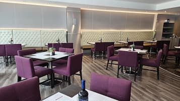 Ein modernes Restaurant mit violetten Sitzmöglichkeiten, Holztischen und einer gepolsterten Sitzgruppe mit Kopfteil.