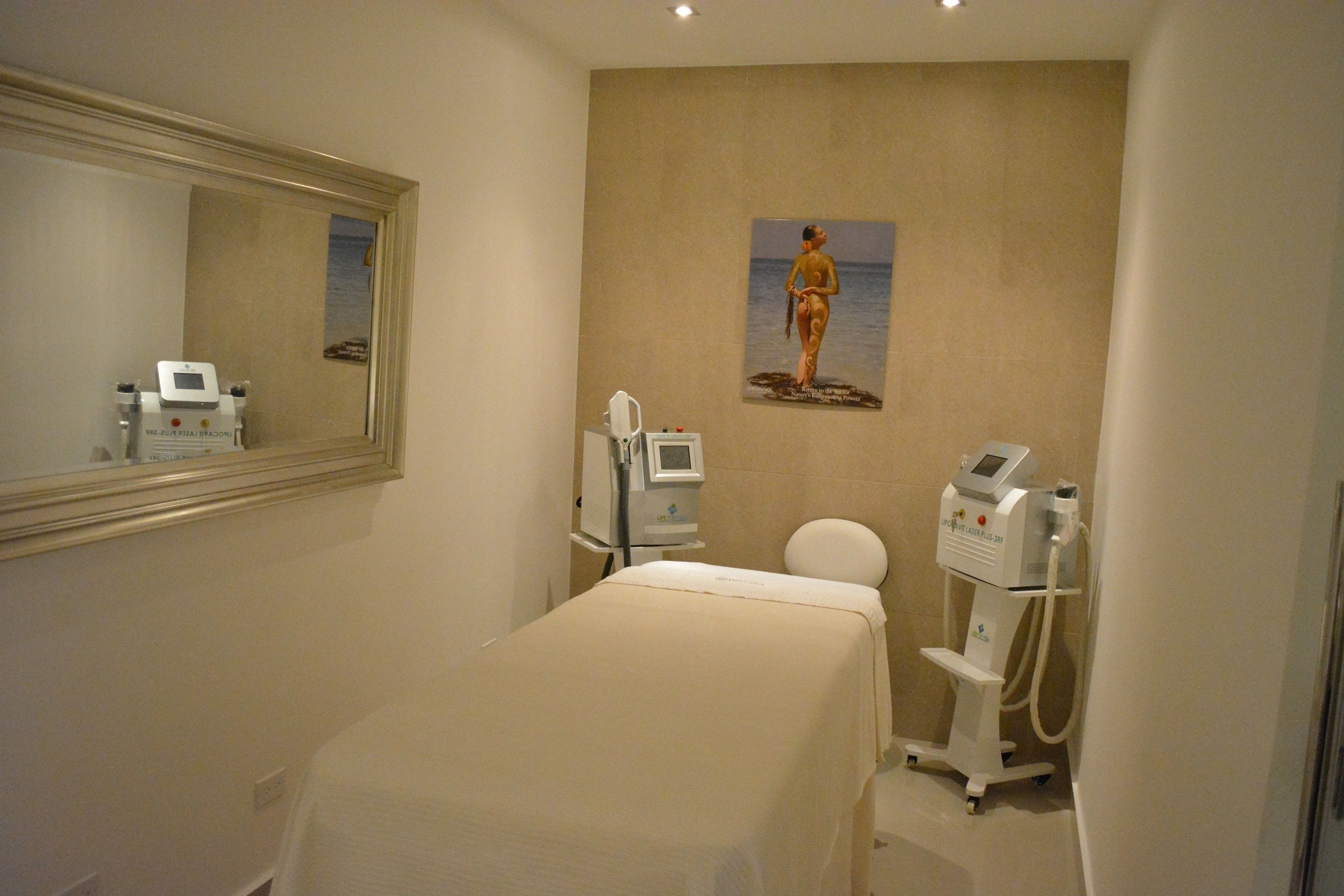 A clinical room with a bed, a medical machine, and a painting of a woman by the sea.