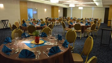 A conference room with multiple round tables, each set with blue napkins, silverware, and wine glasses.