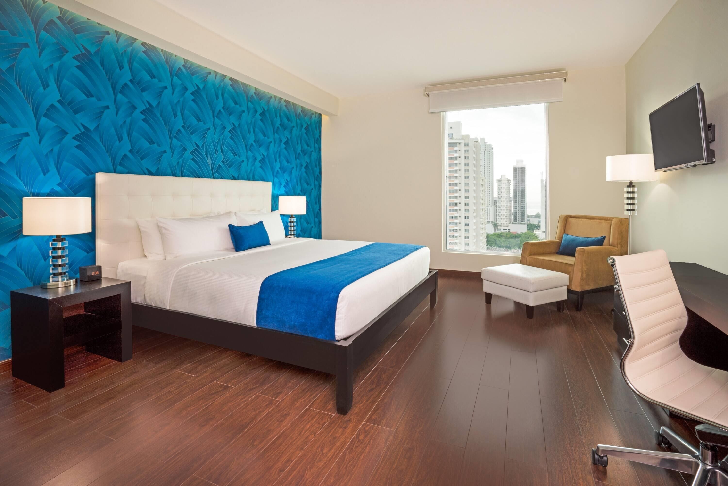 A hotel room with a large bed, a desk, a chair, and a TV.
