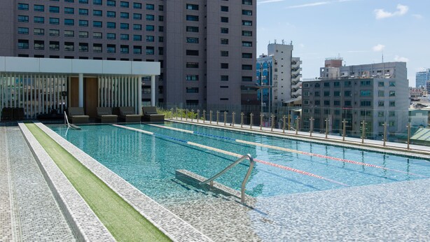 Una piscina con carriles delimitados, rodeada por un edificio moderno y un rascacielos al fondo.