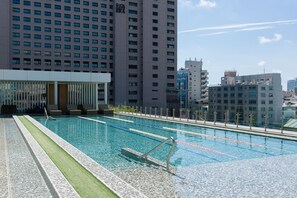 Una piscina con carriles delimitados, rodeada por un edificio moderno y un rascacielos al fondo.