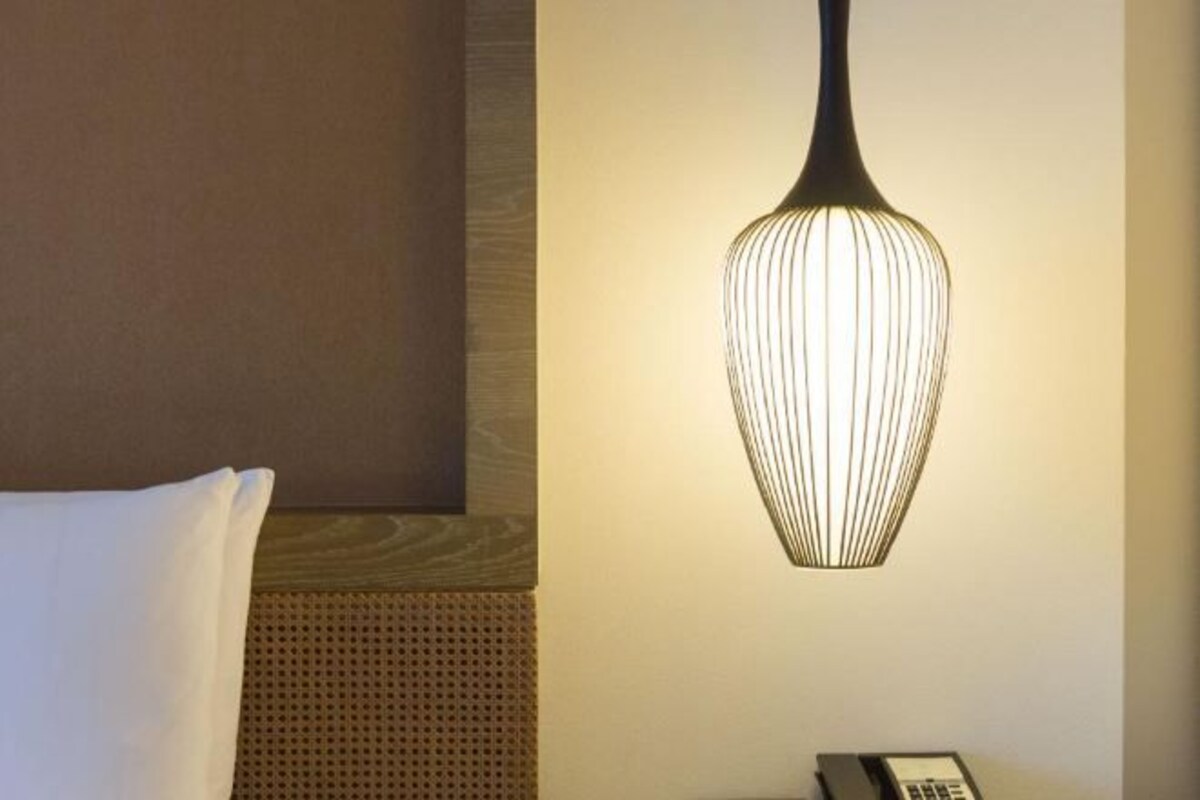 Una habitación de hotel con una cama, un teléfono en la pared y una lámpara colgante.