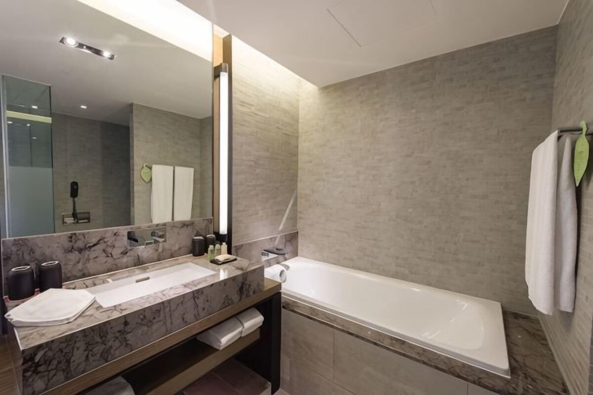 Un baño moderno con un lavabo de mármol, un espejo grande, una bañera y un perchero para toallas.