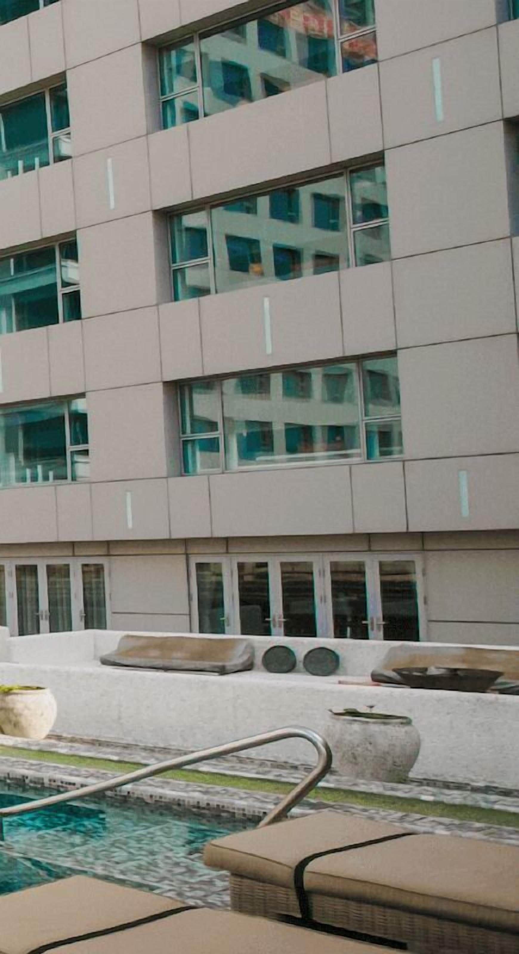 A modern building with multiple windows and a pool area with lounge chairs and a small pool.