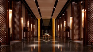 Un pasillo con piso reflectante, separaciones de celosía de madera e iluminación vertical.