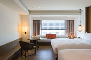 A hotel room with a large bed, a sofa bed, a dining table, and a chair.