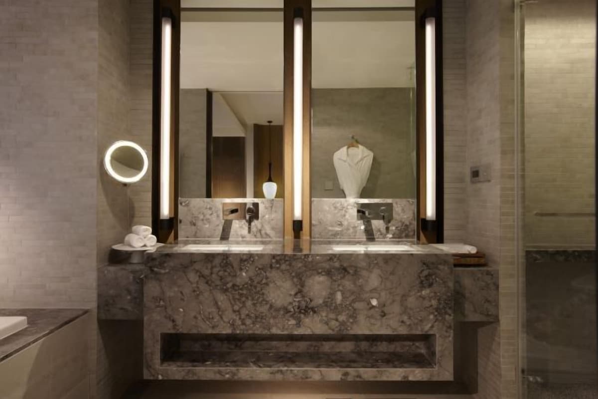 Un baño moderno con tocador de mármol, un espejo grande y una luz de aro.