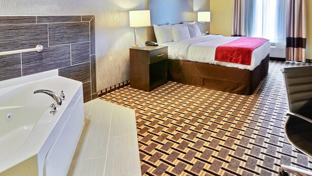 Ein Hotelzimmer mit einem großen Bett, einem eigenen Badezimmer mit Badewanne, einem Schreibtisch und einem Stuhl.