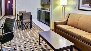Ein Hotelzimmer mit einer Couch, einem Esstisch mit Stühlen, einer Küchenzeile und einem gemusterten Teppich.