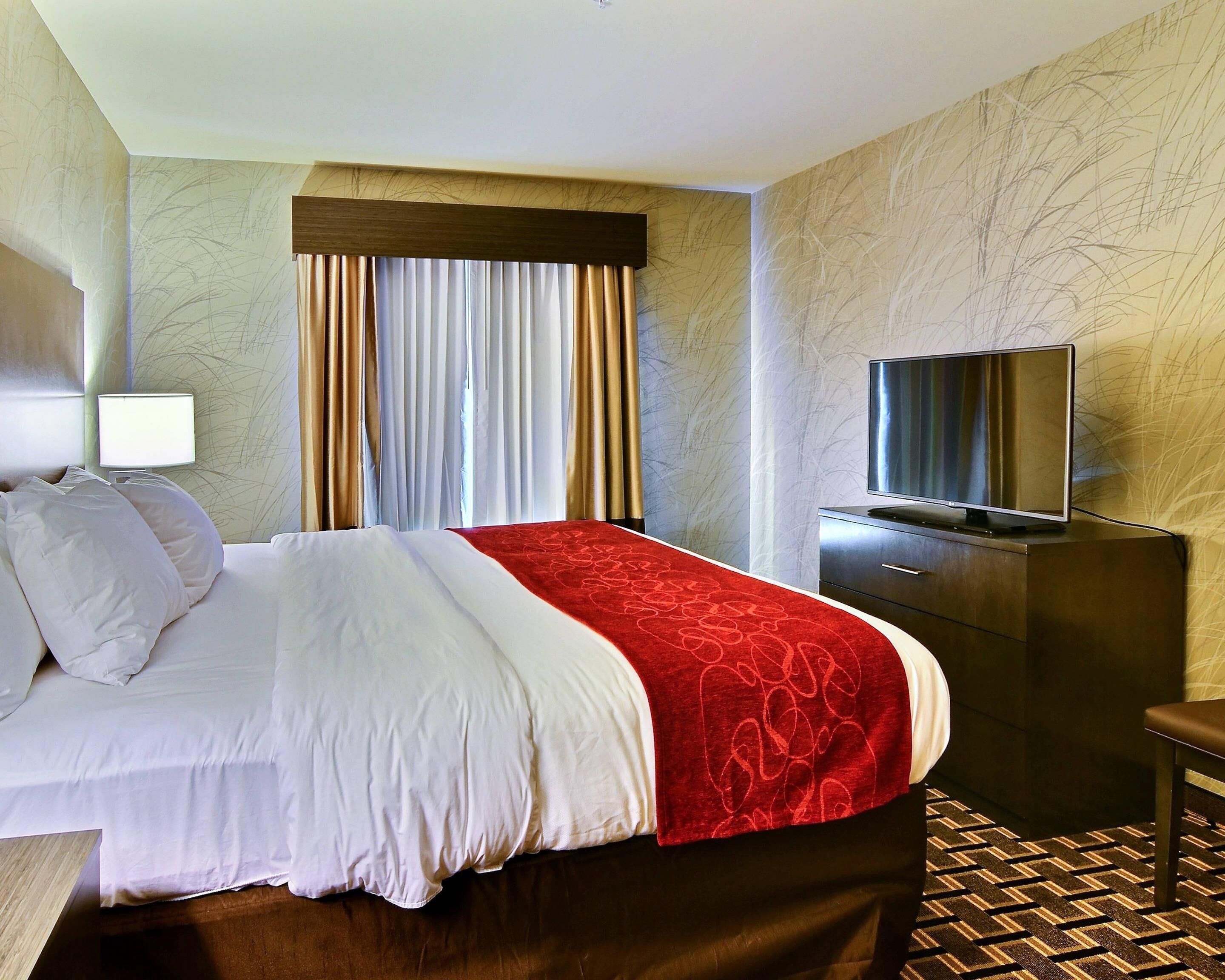 A hotel room with a bed, a TV on a dresser, and a window with curtains.