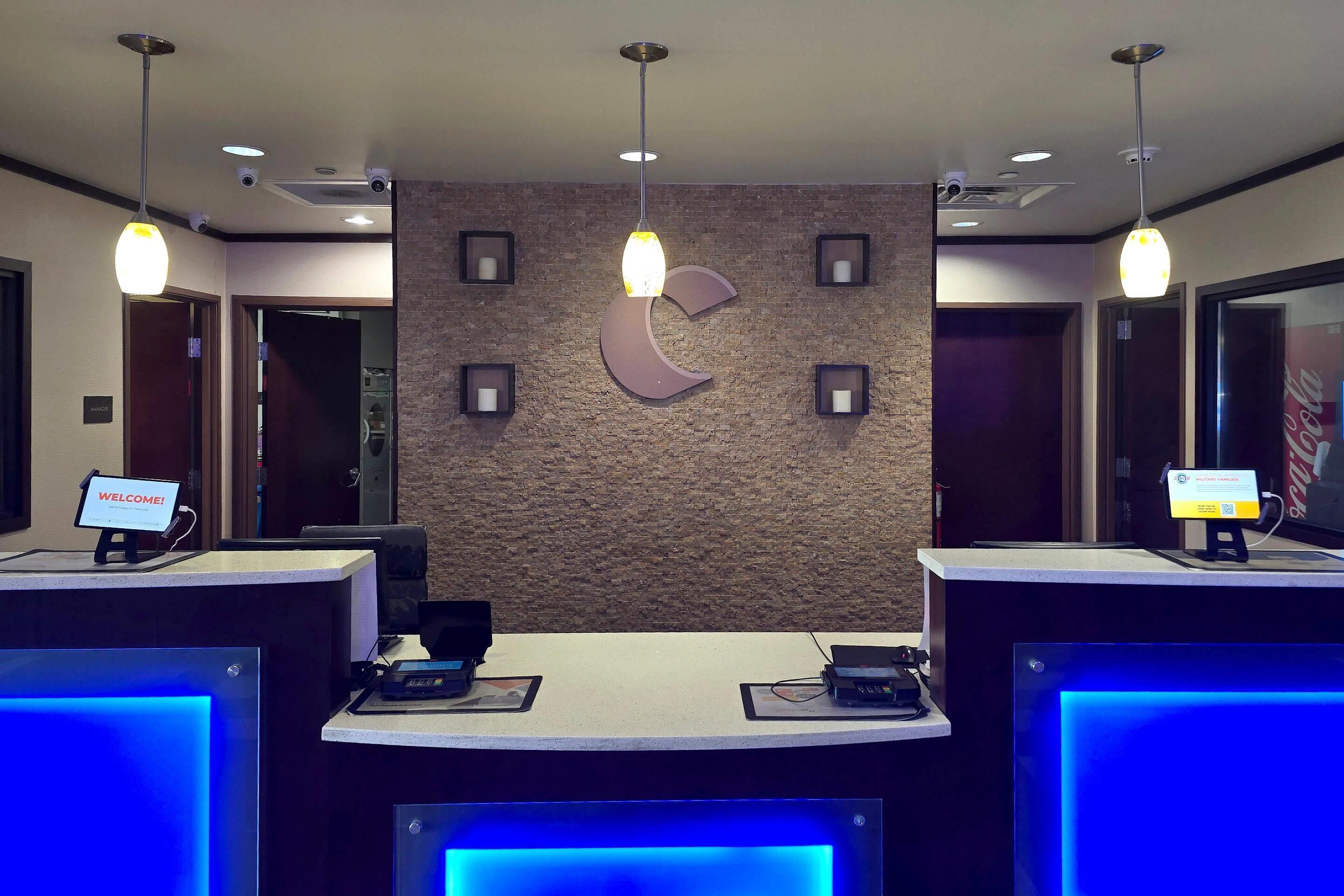 A hotel reception area with a modern design, featuring a central wall with a crescent moon motif, two reception desks with digital displays, and overhead pendant lighting.