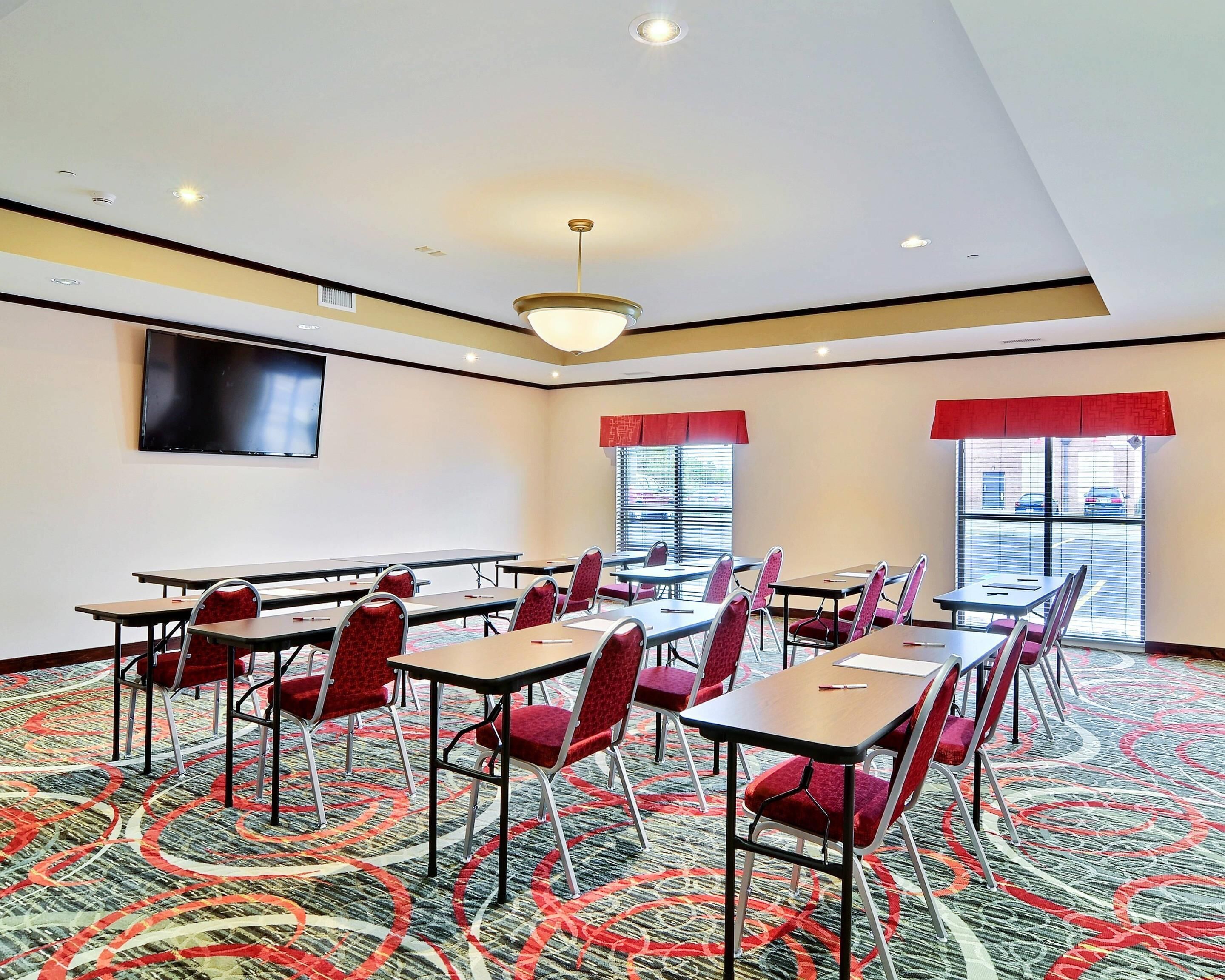 Une salle de conférence dotée d’un grand écran, de plusieurs tables et de chaises rouges.