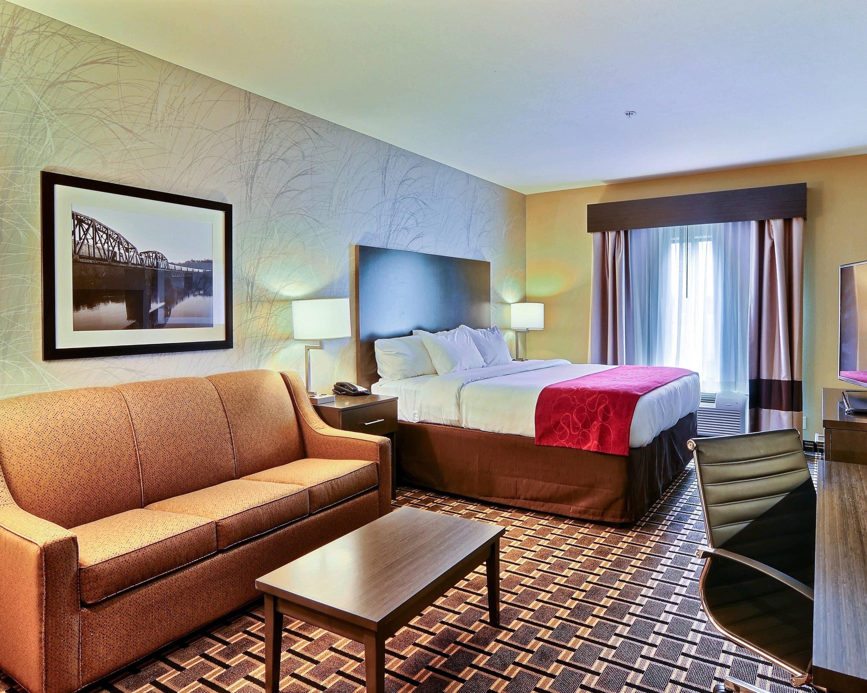 A hotel room with a bed, a sofa, a coffee table, a TV, and a patterned carpet.