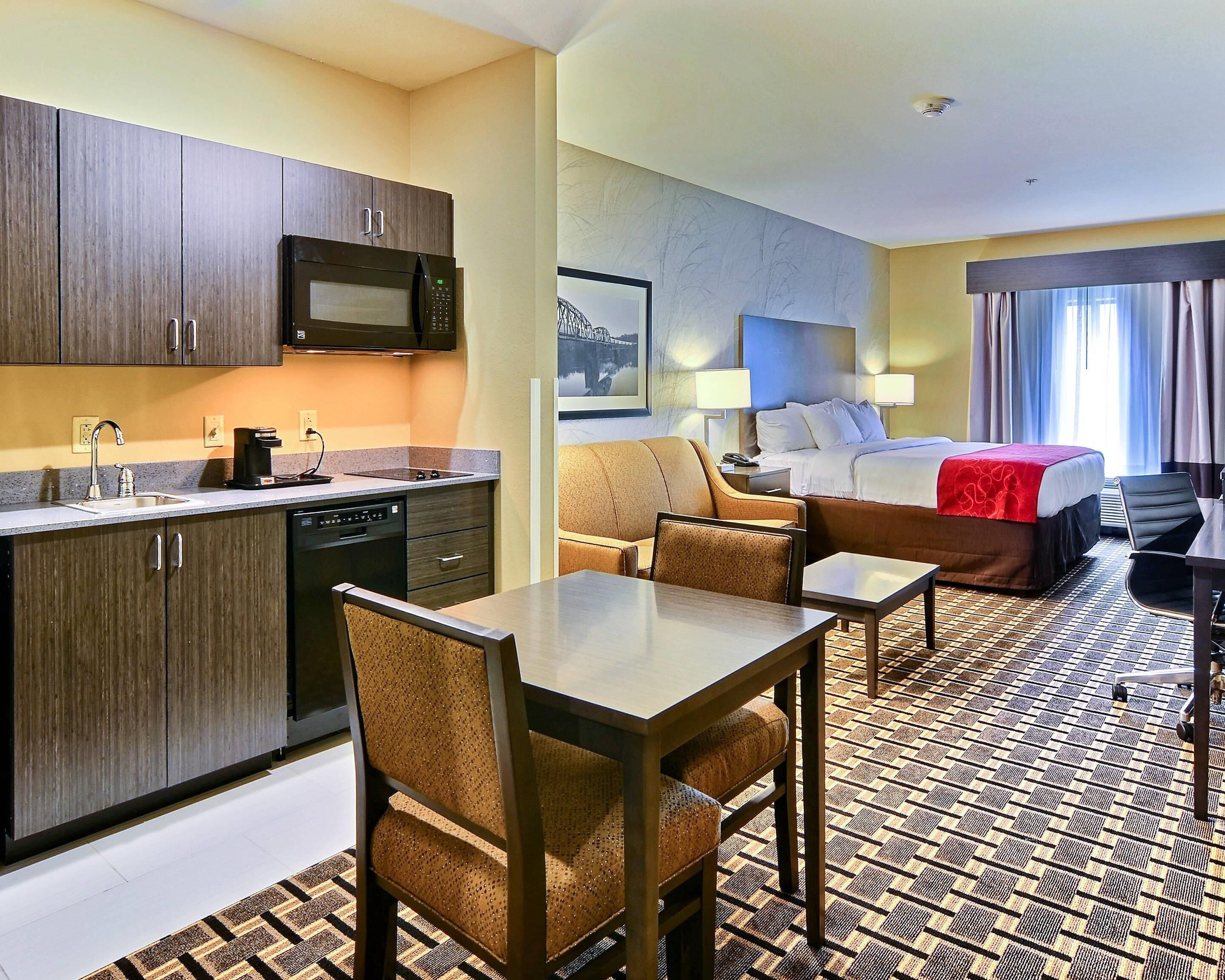 A hotel room with a kitchenette, a bed, a sofa, and a dining area.