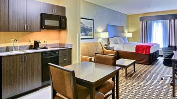 A hotel room with a kitchenette, a bed, a sofa, and a dining area.