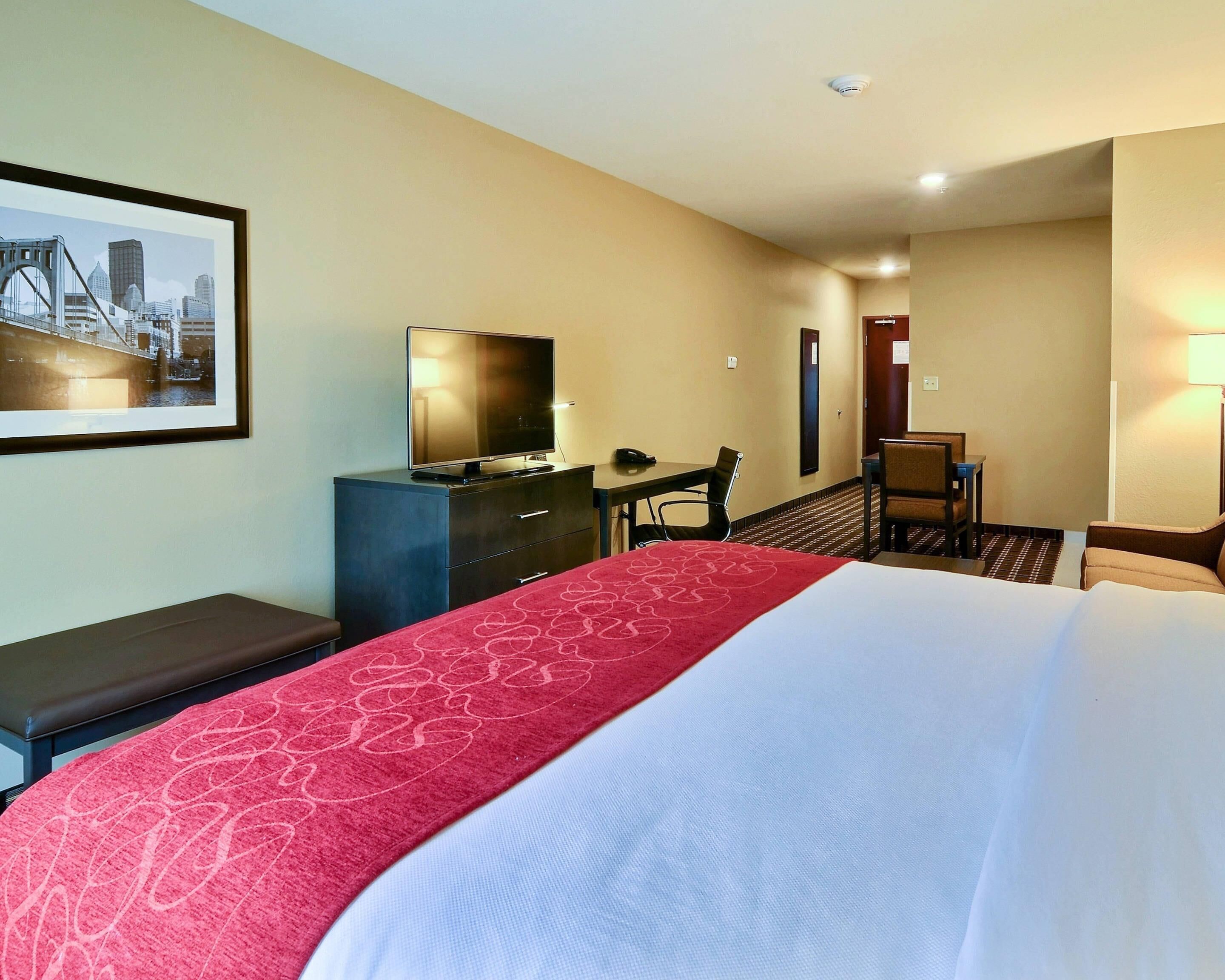 A hotel room with a bed, a desk, a chair, a television, and a framed picture on the wall.