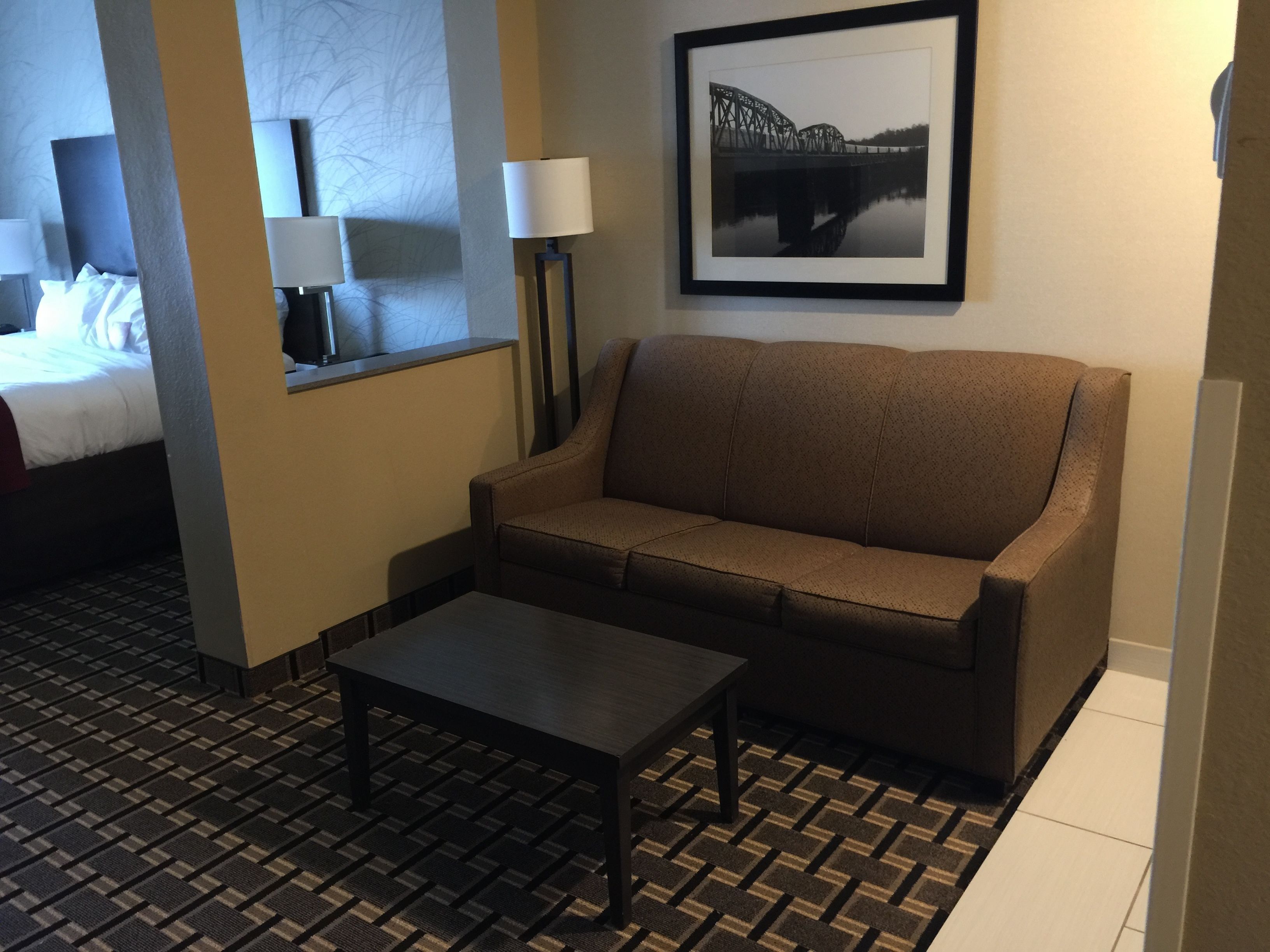 Una habitación de hotel con sofá, una mesita, cama y un cuadro en la pared.