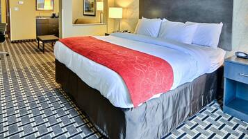 A hotel room with a large bed, a desk, a chair, a mirror, and a bathroom.