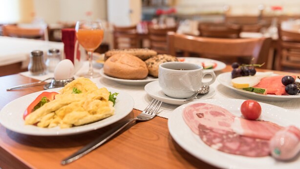 Une table de petit-déjeuner avec des assiettes d’œufs, des toasts et de la viande, une tasse de café et un verre de jus d’orange.
