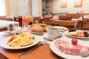 Una tavola imbandita con uova, pane tostato e salumi, una tazza di caffè e un bicchiere di succo d'arancia.