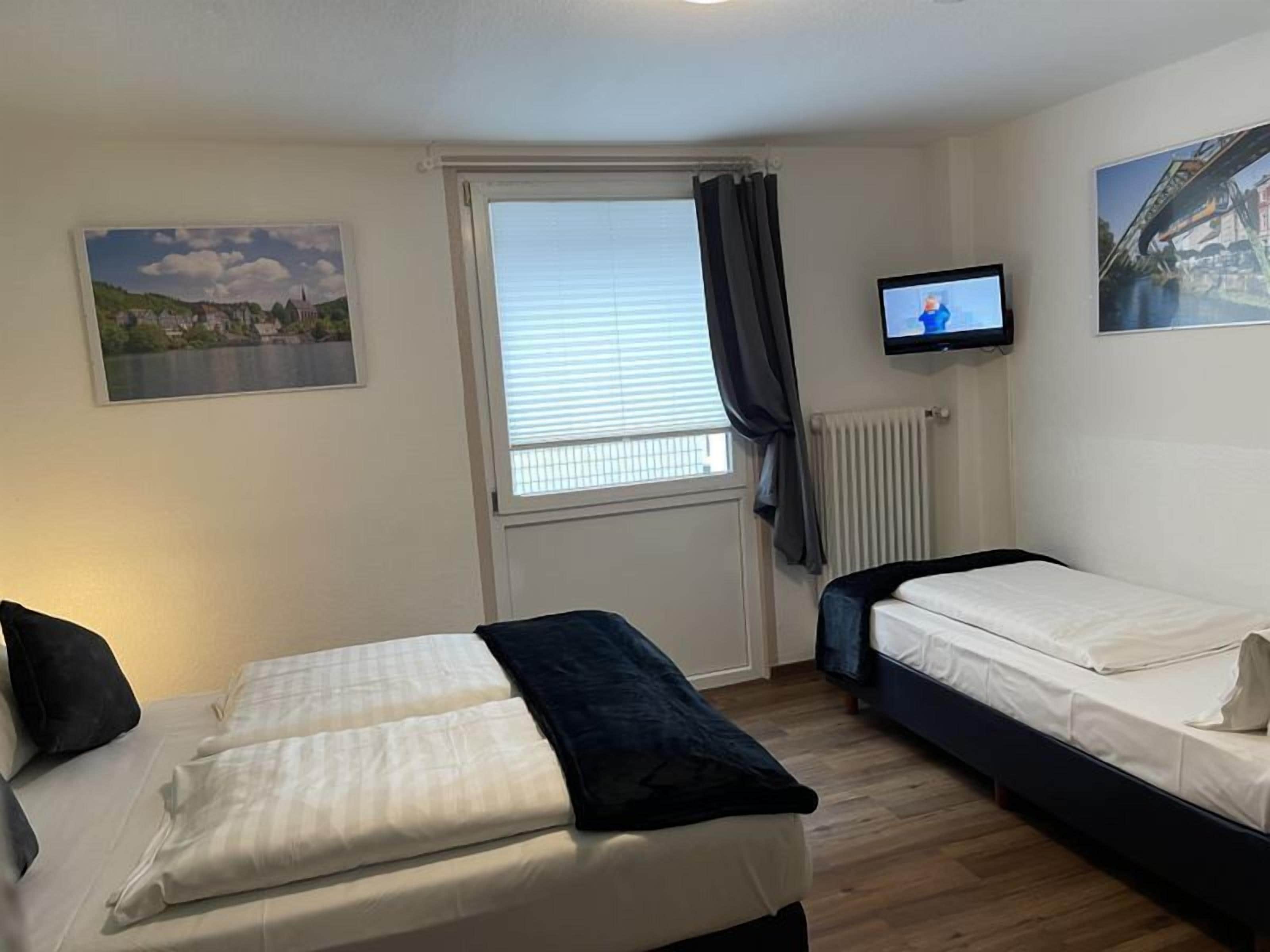 A bedroom with two beds, a television, and a window with curtains.