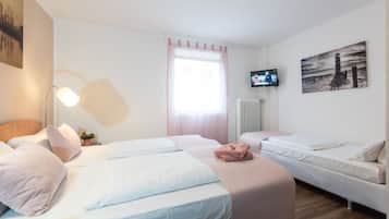 A hotel room with two beds, a TV, a window with curtains, and artwork on the walls.