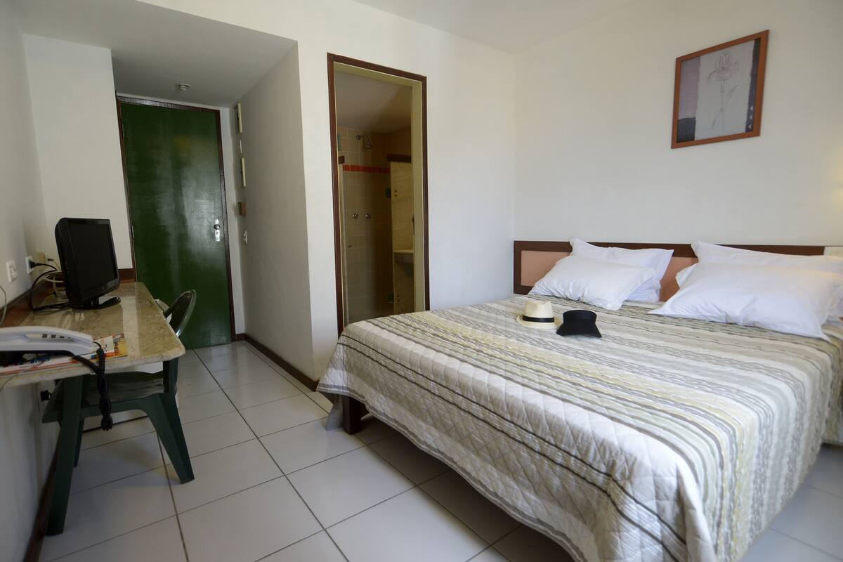 A hotel room with a bed, a desk with a telephone, and a green door leading to a bathroom.