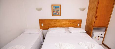 A hotel room with two beds, a wooden headboard, a small refrigerator, and a colorful painting on the wall.