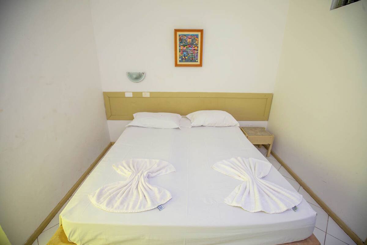 A single bed with a wooden headboard, two pillows, a small bedside table, and a framed picture on the wall.