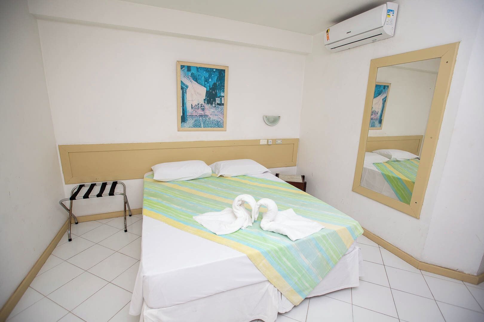 Une chambre d’hôtel comprenant un lit, une table de chevet, un miroir et un climatiseur fixé au mur.