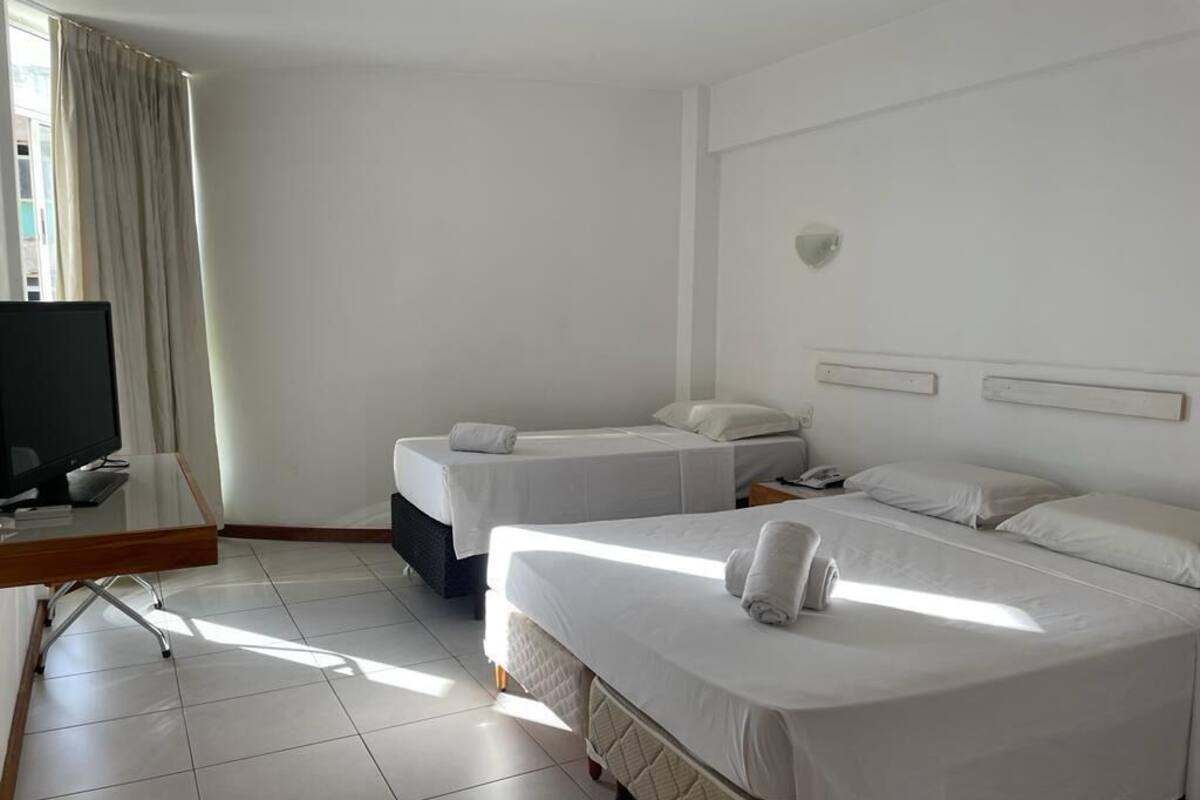 A hotel room with two beds, a desk with a computer, and a window with curtains.