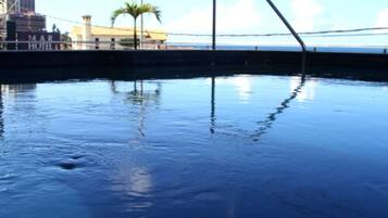 Piscina com escada de metal, palmeira e um edifício com a inscrição "MAR HOTEL" ao fundo.