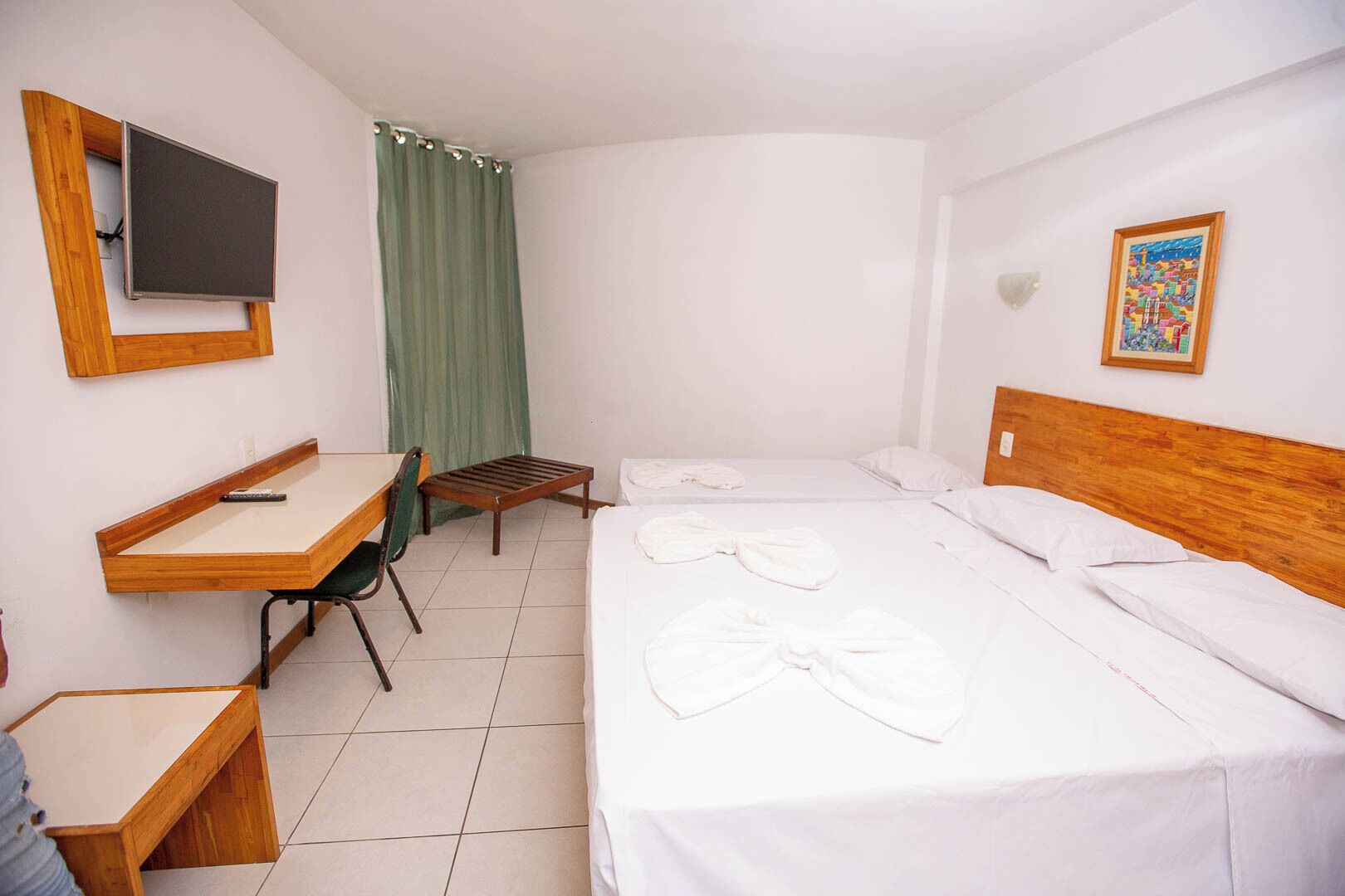 A hotel room with a bed, a desk, a chair, a television, and a painting on the wall.
