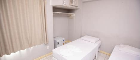 A small, clean room with a single bed, a bedside table, a heater, and a window with curtains.