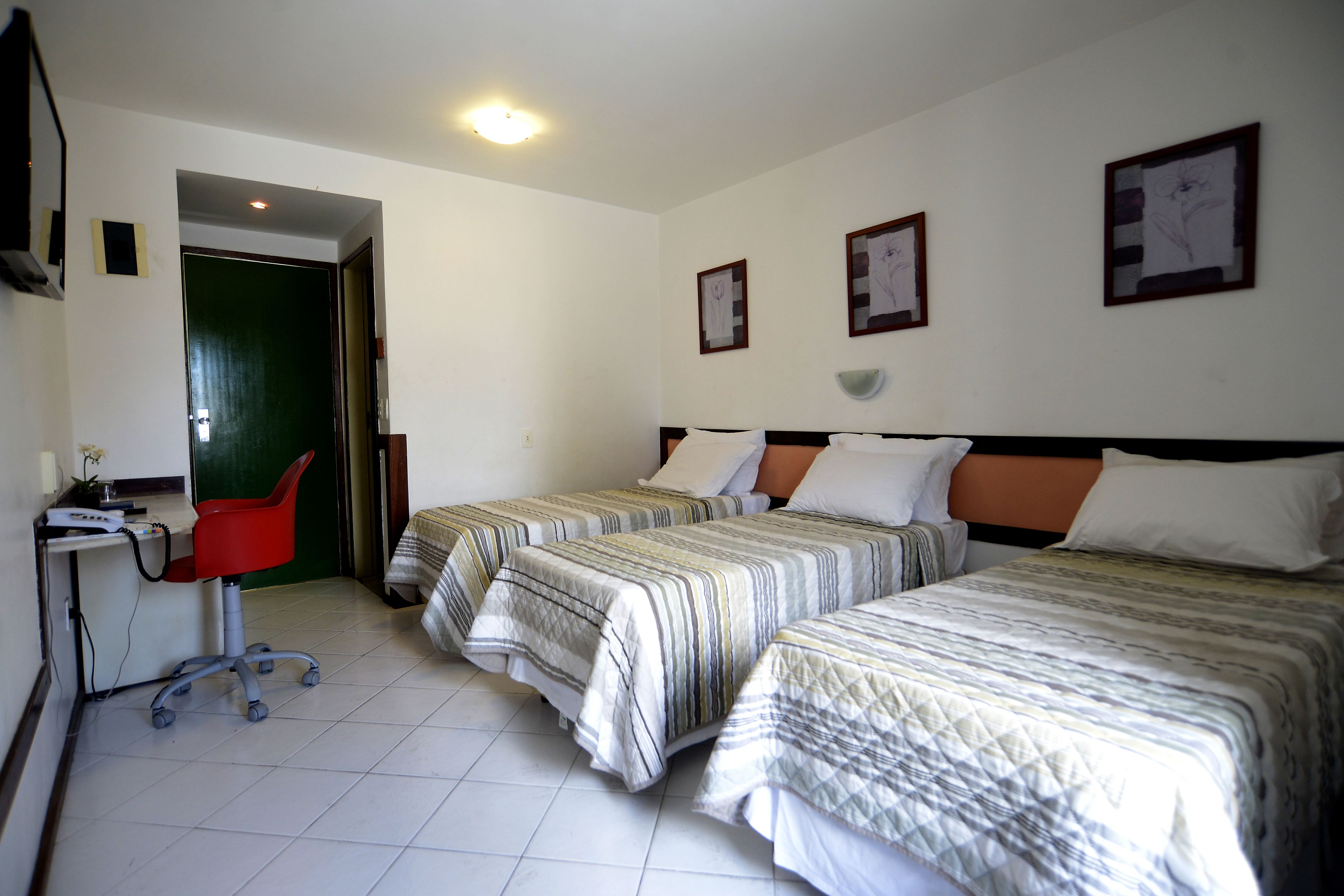 Ein Hotelzimmer mit zwei Betten, einem Schreibtisch und einem Stuhl. An der Wand hängen gerahmte Bilder.