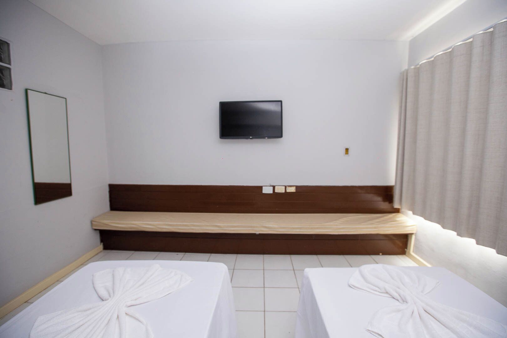 A hotel room with a bed, a television mounted on the wall, and two bedside tables with towels.