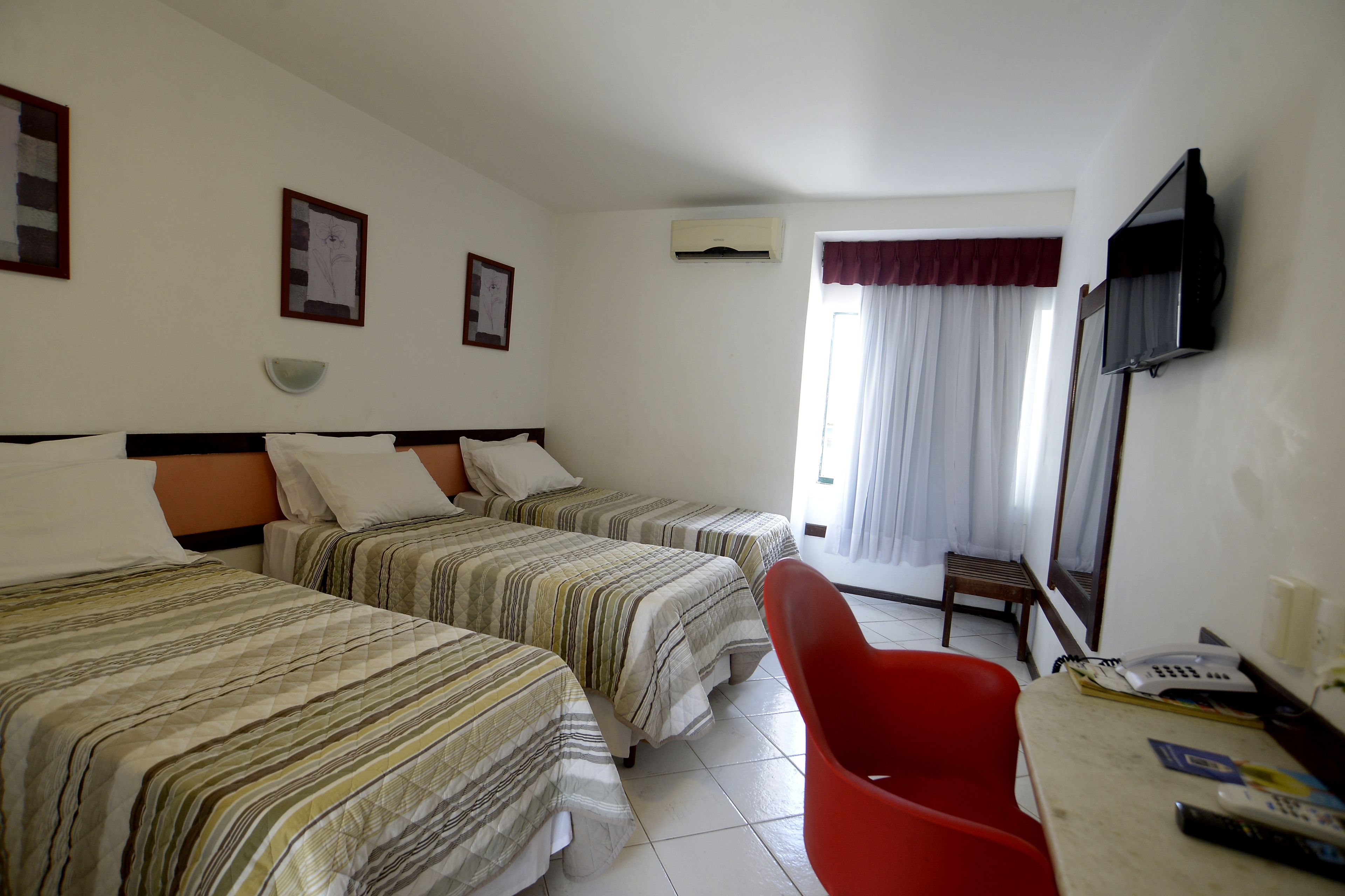 A hotel room with two beds, a TV, a desk with a chair, and a window with curtains.