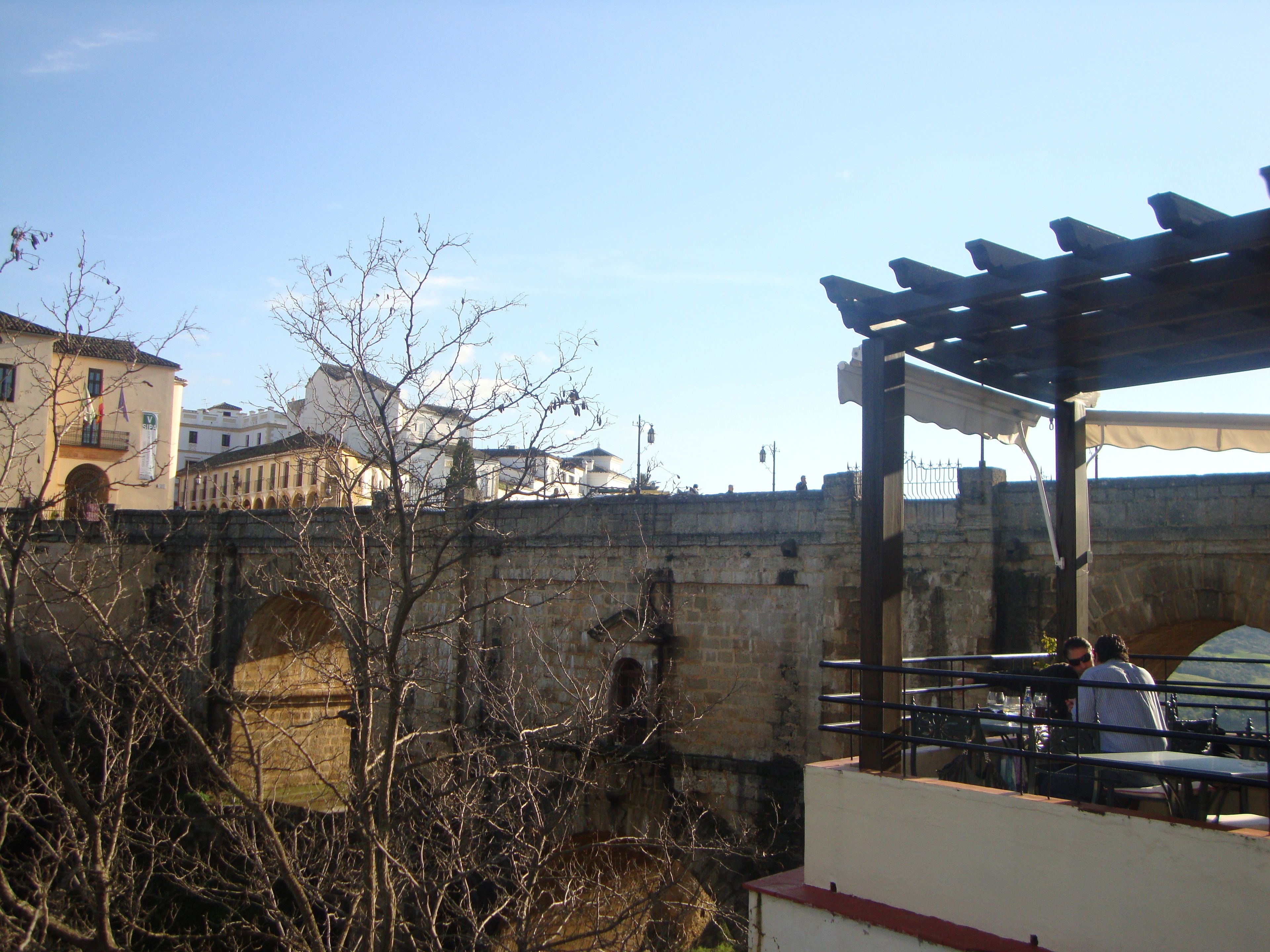 A stone bridge with a restaurant patio overlooking a cityscape.