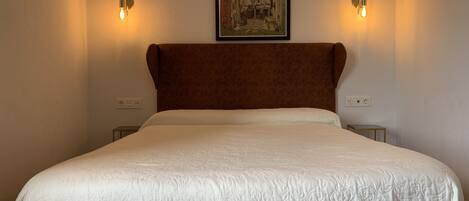 Un dormitorio con una cama grande, dos lámparas fijadas a la pared y un cuadro enmarcado sobre la cama.