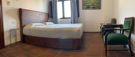Una habitación de hotel con una cama, un escritorio, una silla y un cuadro en la pared.