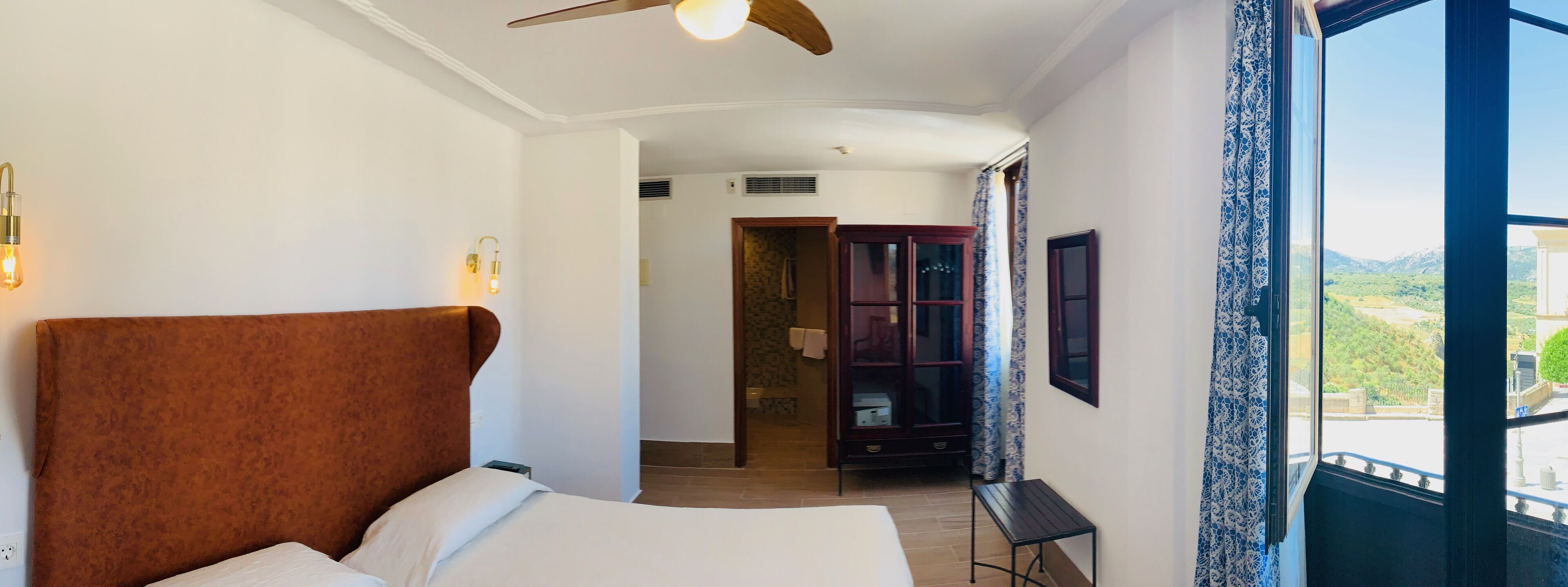 A hotel room with a large bed, a ceiling fan, a view of the outdoors, and a wooden cabinet.