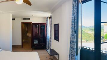 Una habitación de hotel con una cama grande, un ventilador de techo, vistas al exterior y un armario de madera.