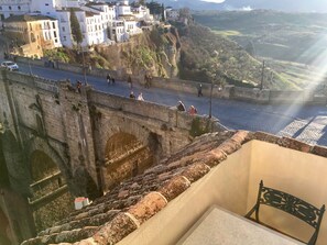 A stone bridge with people walking on it, overlooking a town with white buildings and a view of the countryside. - Hotel Don Miguel (Ronda)