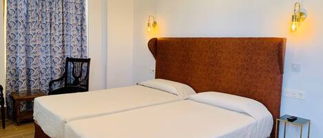 A double bed with a wooden headboard, two bedside lamps, a small table, and a chair.
