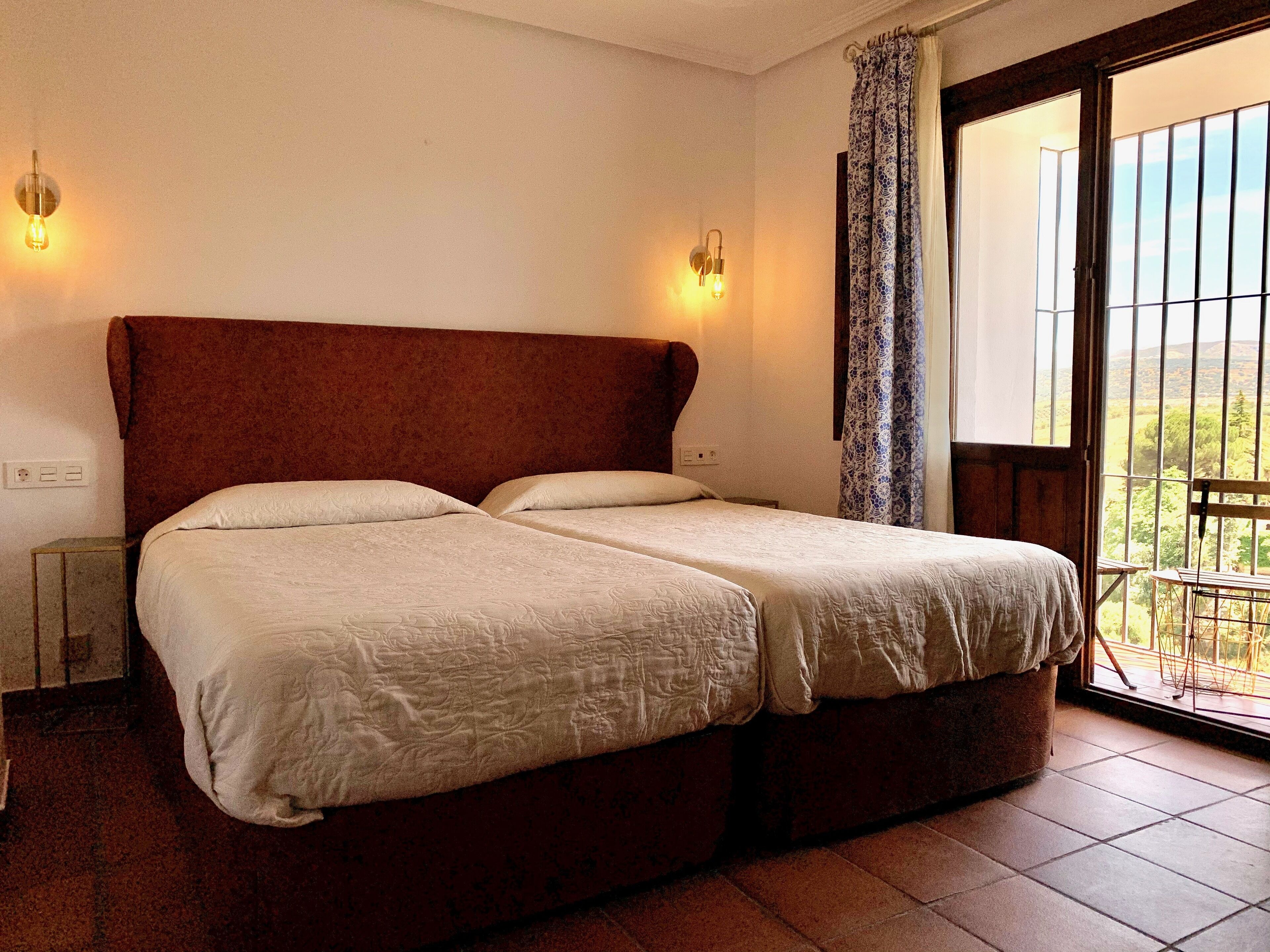 A double bed with a wooden headboard, two bedside lamps, and a view of the outdoors through a large window.